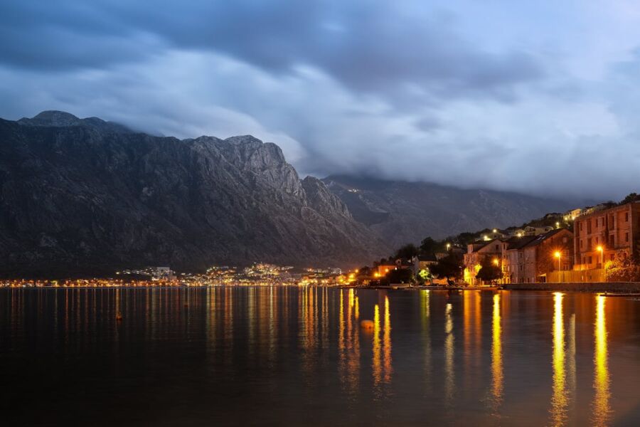 Lakeside village at twilight with mountain reflections, cozy lights, and serene water.