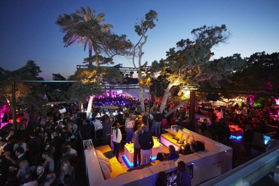 Twilight outdoor party scene with a lively crowd, chic lounge, vibrant lights, and tropical vibe.