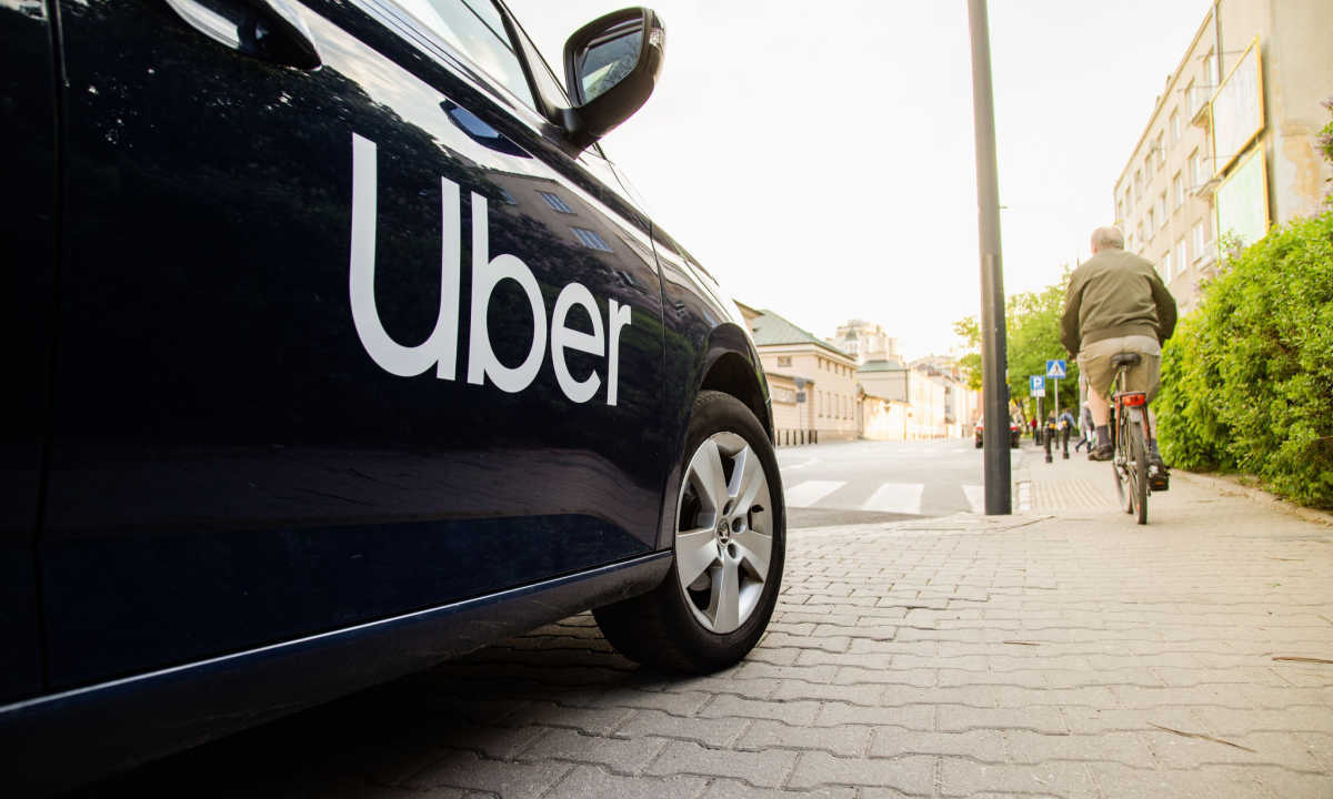 Uber car parked in city street with cyclist and cobblestone sidewalk.