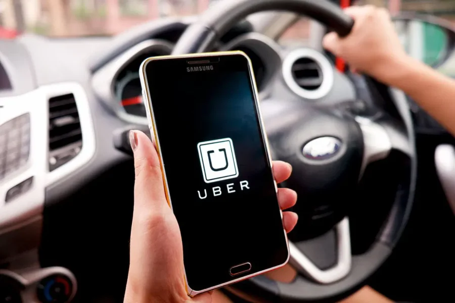 Uber app displayed in car interior with steering wheel and dashboard visible.