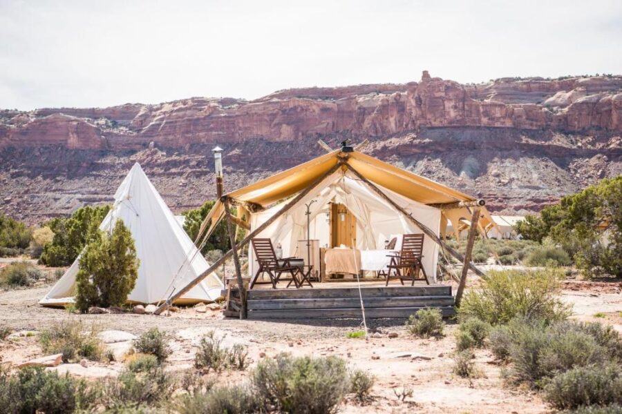 Desert scene at Under Canvas Moab, Utah, showcasing a tent with a table and chairs arranged nearby.
