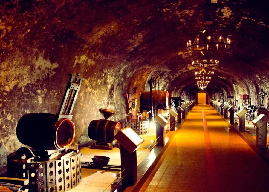 Underground Reims champagne cellar displaying antique winery barrels and winemaking machinery.