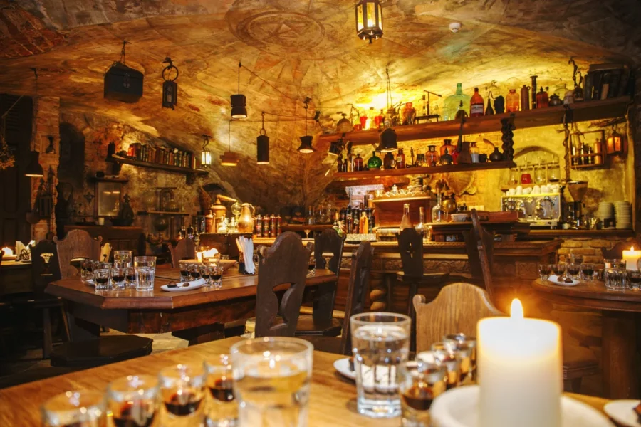Candlelit underground stone tavern with wooden tables and Riga Black Balsam bottles.