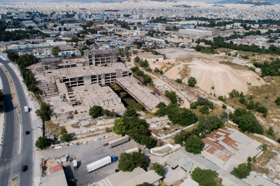Drone aerial of abandoned unfinished concrete building and industrial yards on urban outskirts.