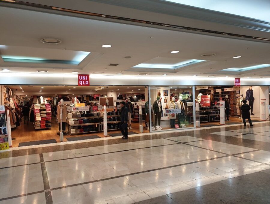 UNIQLO clothing store in modern indoor shopping mall with mannequins, winter apparel displays, and shoppers.