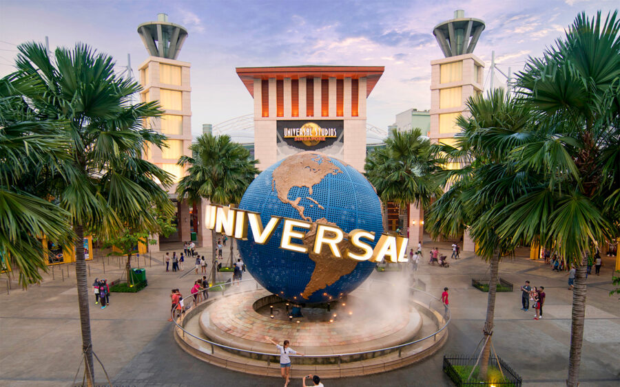 Universal Studios entrance with globe, fountain, palm trees, modern architecture, and excited visitors.