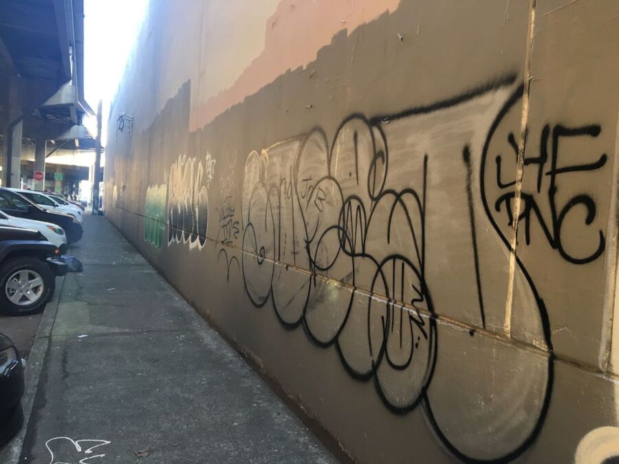 Graffiti-filled urban alley with parked SUVs and weathered walls.