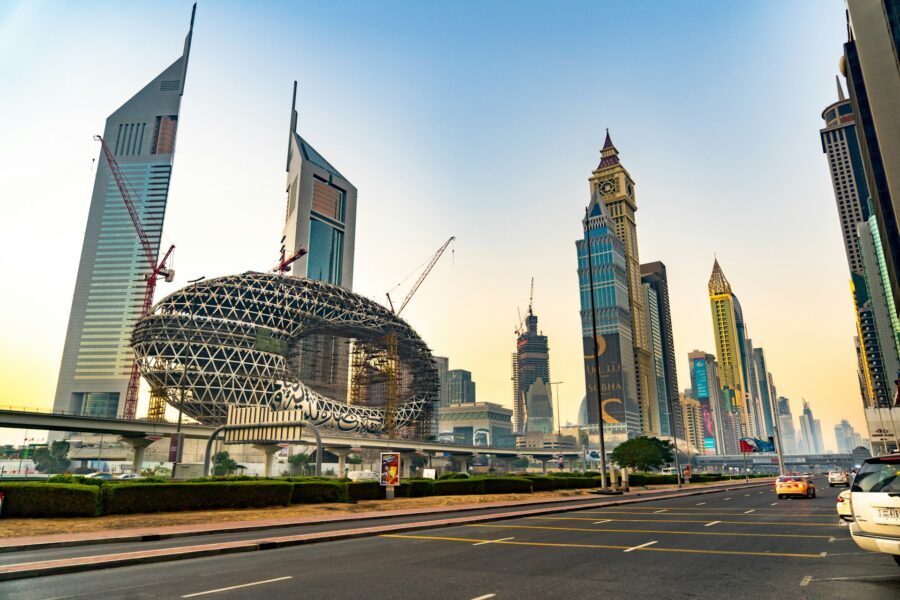 Futuristic urban skyline with skyscrapers, construction cranes, roadway, and pastel sky at dusk.