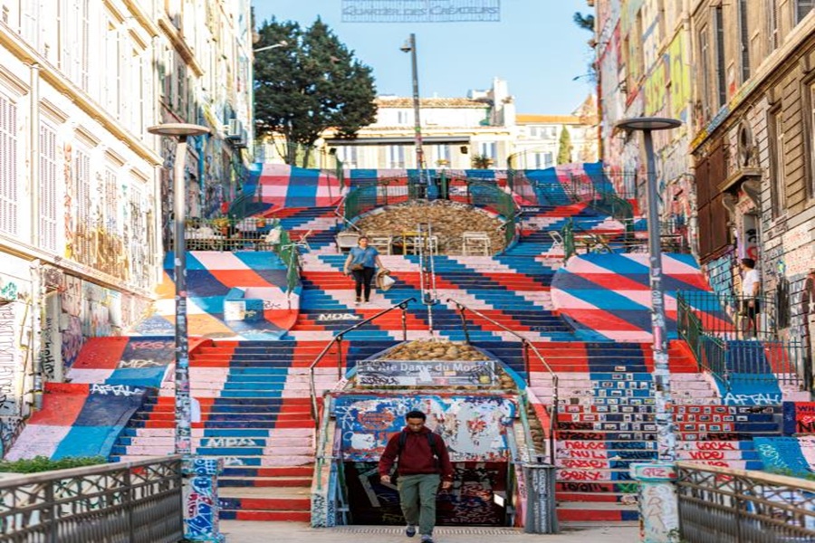 Colorful urban staircase with graffiti, people walking, and diverse architectural surroundings.
