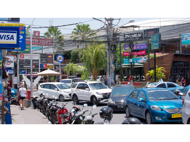 Urban street with tropical charm, busy traffic, vibrant businesses, and palm trees.