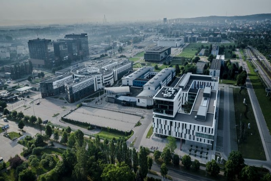 Aerial view of modern urban landscape with sleek buildings, greenery, and parking lot.