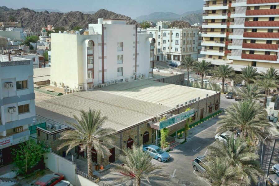 Muttrah Muscat hotel and apartments with palm trees against rocky desert mountains under clear sky.