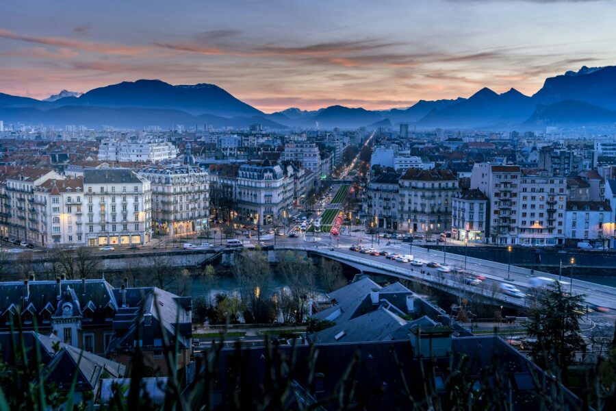 Grenoble skyline at twilight with river, bridge, and avenue leading to mountains.