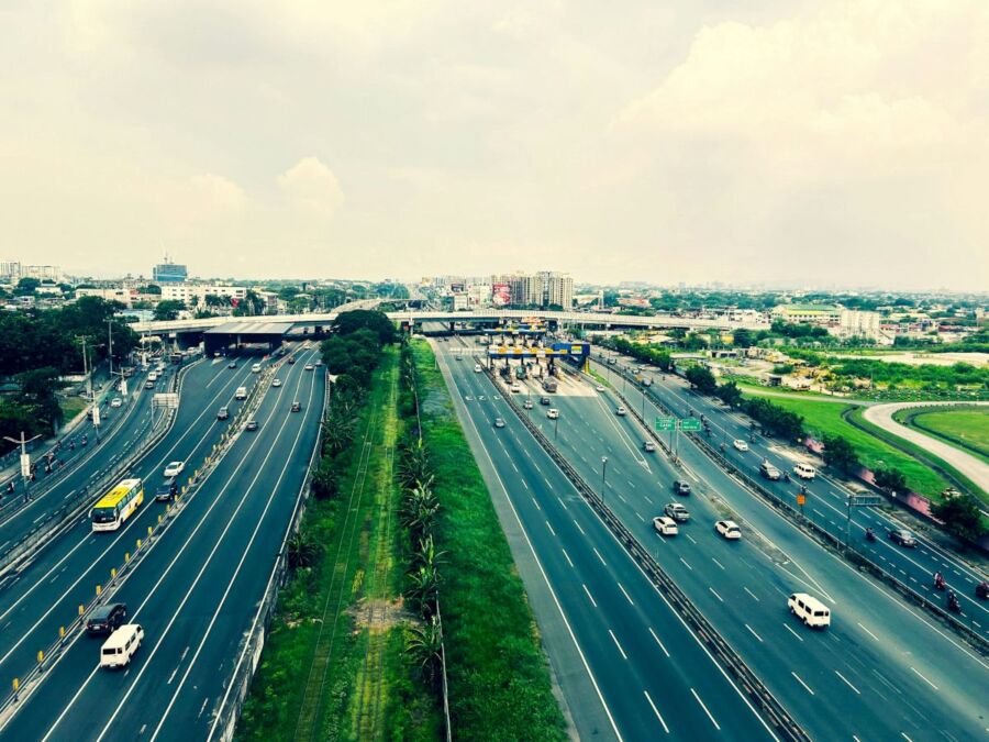 Busy urban highway with diverse traffic, public transport, and surrounding cityscape.