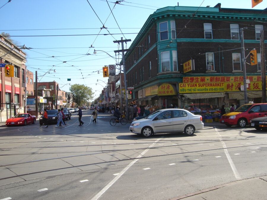 Bustling urban intersection with cars, pedestrians, cyclists, historic architecture, and vibrant street life.