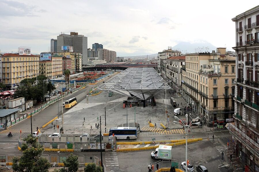 Napoli Centrale cityscape showing modern hub, historic buildings, vibrant life, and Mount Vesuvius in background.