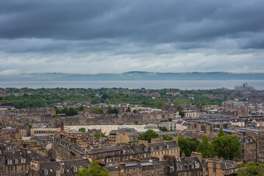 Coastal cityscape: urban architecture, lush greenery, calm sea, cloudy sky, historic charm.