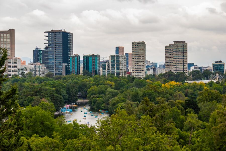 City skyline with lush greenery, waterway, and boats under an overcast sky.