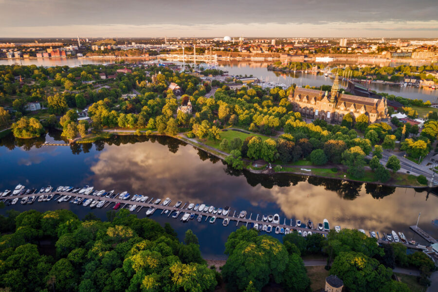 Aerial view of Stockholm: lush greenery, marina, historic architecture, and city skyline at dawn.