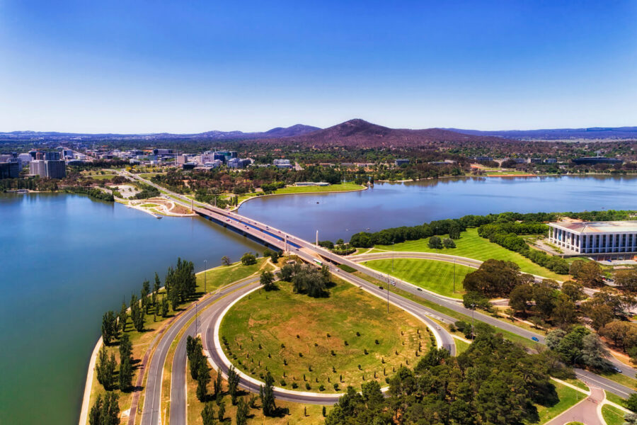 Aerial view of Canberra: lush parks, scenic lake, modern bridge, and skyline.