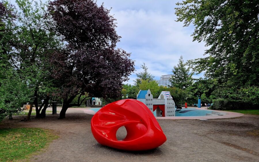 Red glossy abstract sculpture in urban park playground with childrens playhouses.