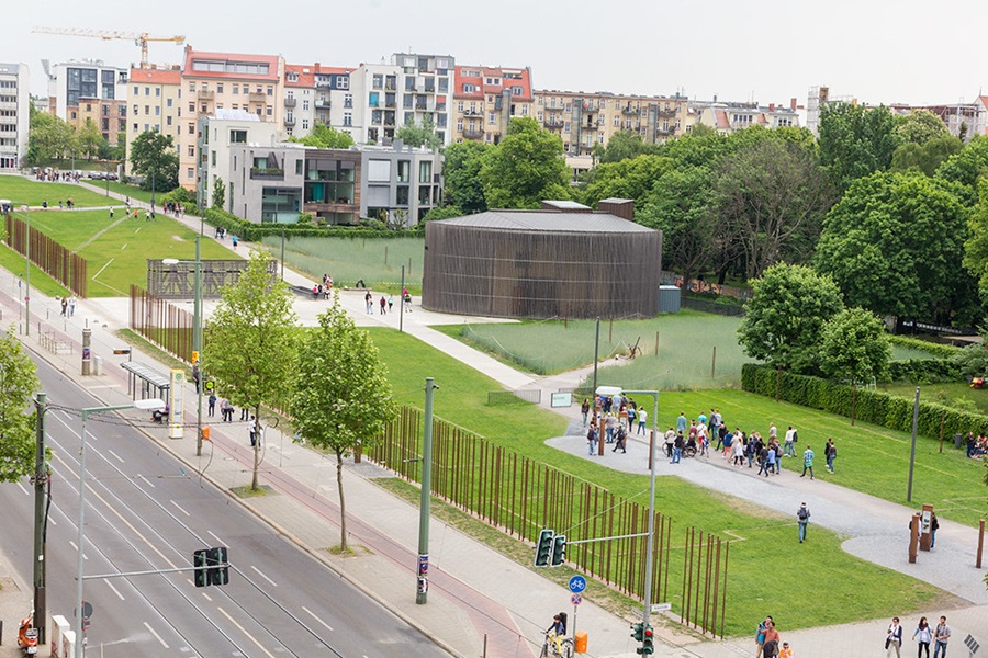 Bernauer Strasse memorial park with dark pavilion, tramway, pathways, and surrounding apartments.