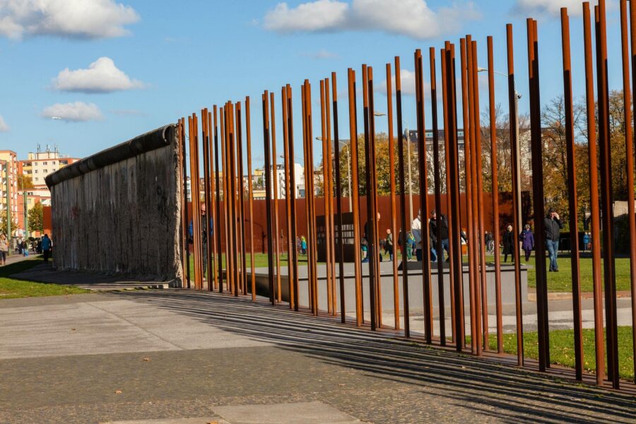 Berlin Wall Memorial: rusted steel posts, concrete slab, long shadows in urban plaza.