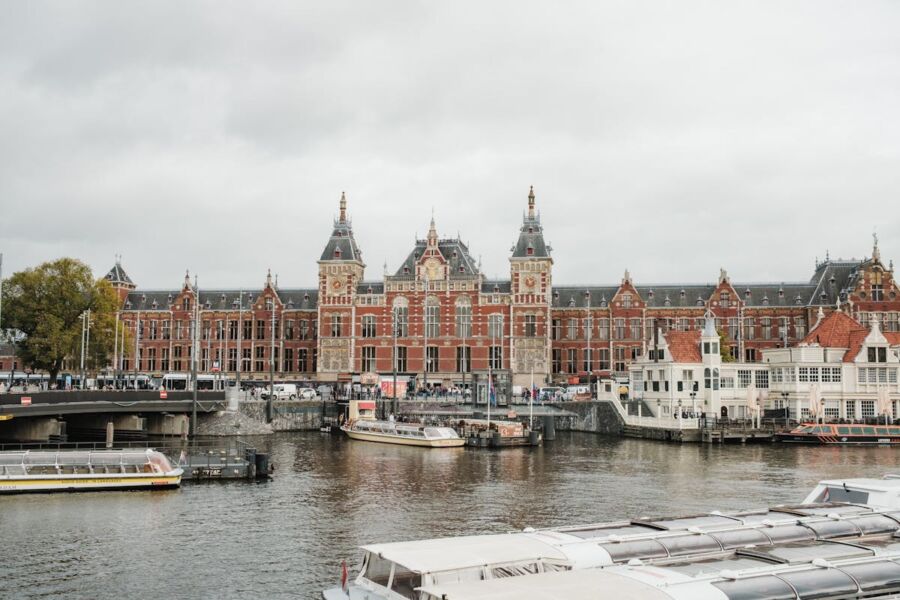 Historic waterfront building with boats, urban skyline, tourists, and vibrant activities under cloudy skies.