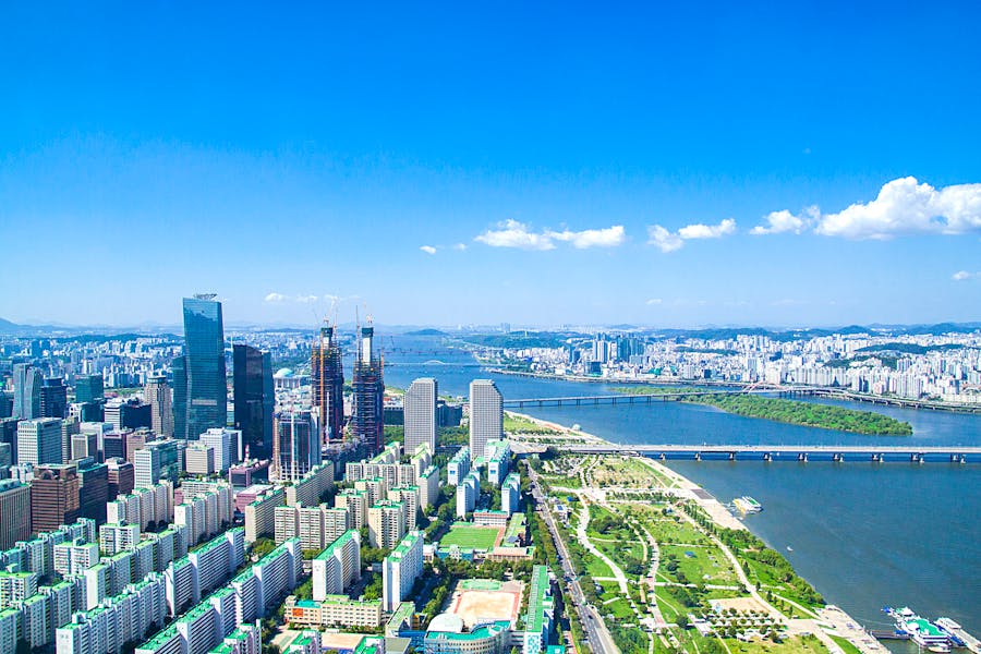 Aerial view of vibrant urban skyline with skyscrapers, river, bridges, and lush green spaces.