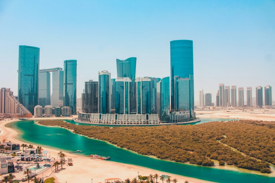 Modern Abu Dhabi skyline with skyscrapers, turquoise waterway, and sandy beach.