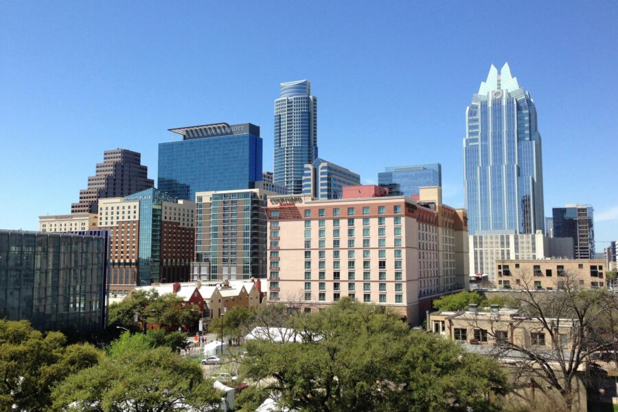 Modern urban skyline with high-rise buildings, greenery, and a clear blue sky.