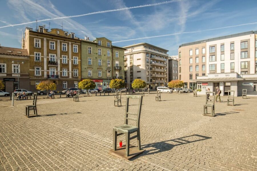 Public square art installation with wooden chairs, historic and modern buildings, sunny atmosphere.