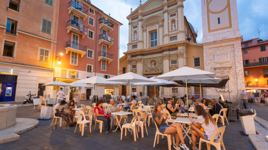 Evening square scene with church, clock tower, dining patrons, and vibrant architecture.