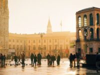 Urban square at golden hour, featuring Gothic cathedral, modern architecture, and diverse crowd.
