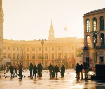 Urban square at golden hour, featuring Gothic cathedral, modern architecture, and diverse crowd.