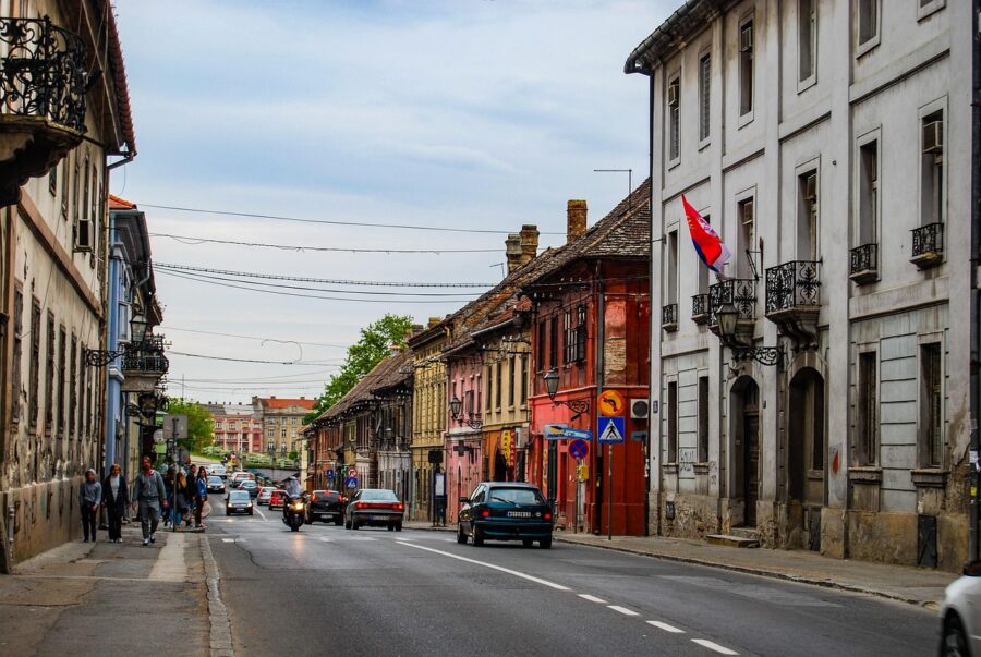 Novi Sad historic street with colorful old European buildings, cars, and pedestrians.