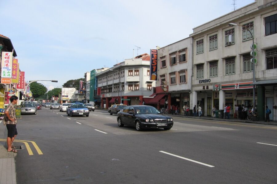 Urban Geylang street scene with shops, cars, and pedestrians, highlighting cultural diversity and modernity.