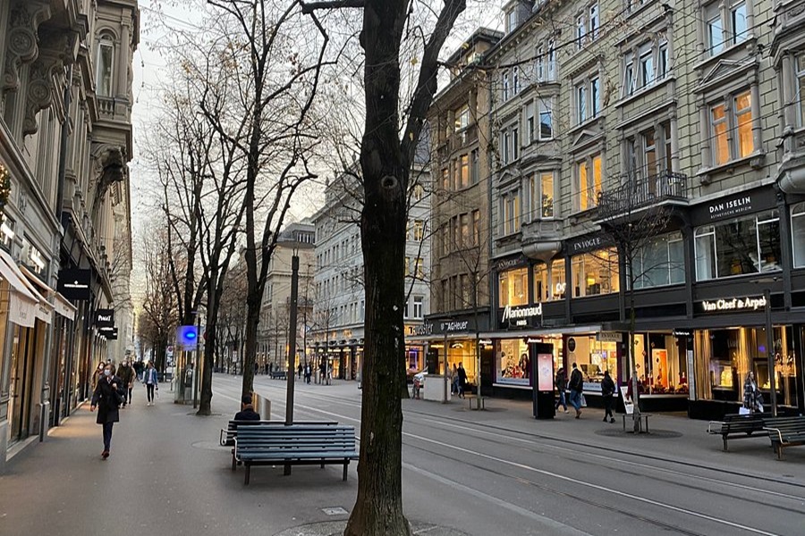 Elegant urban street scene with luxury shops, pedestrians, tram tracks, and European architecture.