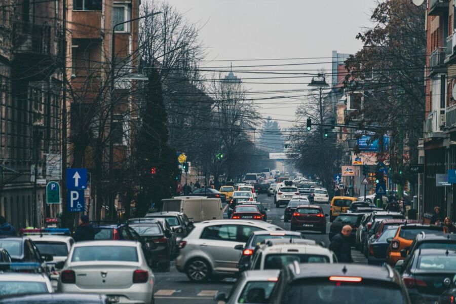 Heavy urban traffic scene with cars, pedestrians, and historical buildings on an overcast day.