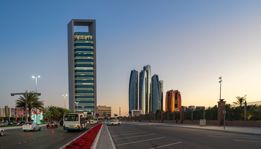 Abu Dhabi skyscraper skyline at dusk, modern architecture, palm trees, vibrant urban scene.