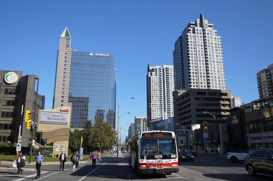 Bustling urban street with city bus, pedestrians, modern Toronto skyline, and clear blue sky.
