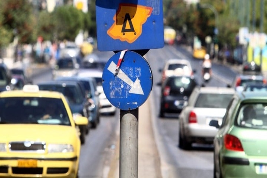 Urban traffic scene with yellow taxi, caution sign, and directional arrow in busy city.