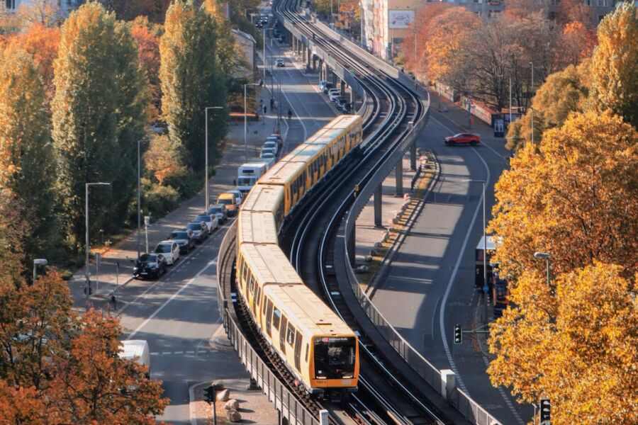 Autumn urban scene with yellow train on elevated track, vibrant foliage, buildings, and streets below.
