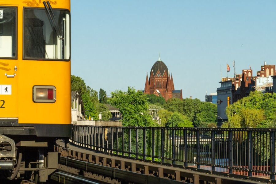 Yellow train in urban landscape with historical architecture and lush greenery.