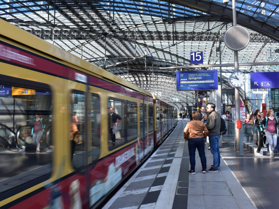 Modern urban train station with skylight roof, vibrant train, commuters, and schedule display board.