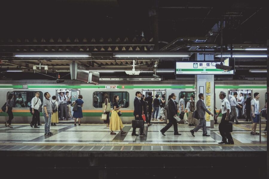 Bustling urban subway station with diverse commuters and green-orange train under modern architecture.
