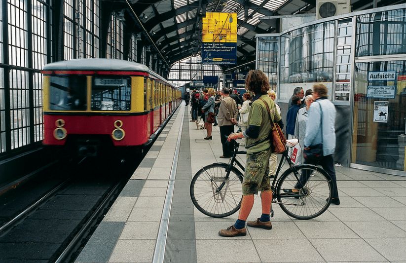 Urban train station scene with commuters, retro train, bicyclist, and modern architecture.