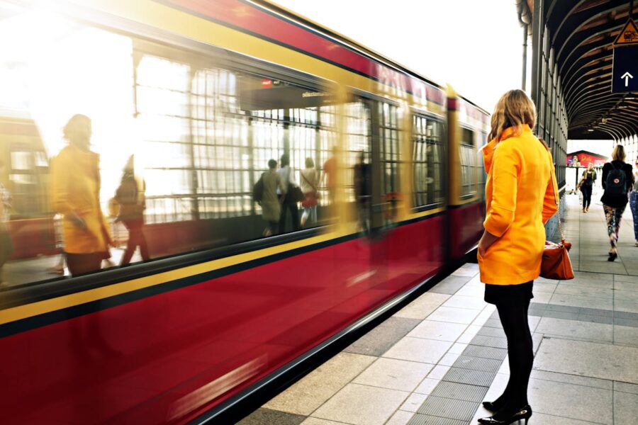 Woman in orange coat at bustling urban train station.