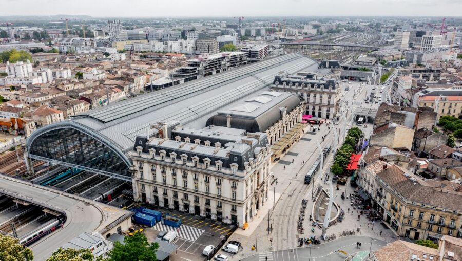 Bustling urban train station with modern and historical architecture, transportation hub, and city life.