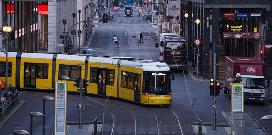 Yellow tram turning at a busy urban intersection at dusk with modern buildings and pedestrians.